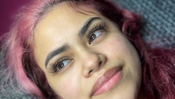 Woman with pink hair and natural-looking eyelash extensions looking up, with a hint of a smile.