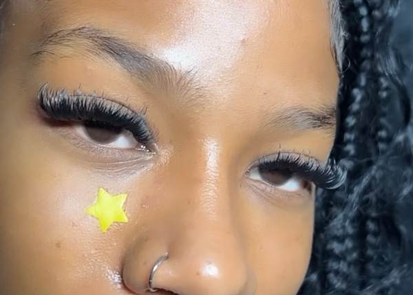 Close view of a woman's face with luxurious eyelash extensions and a small star sticker on her cheek